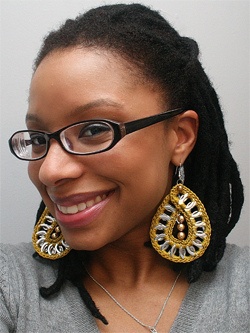 a woman with glasses wearing large gold and silver earring designs on her ears, smiling at the camera