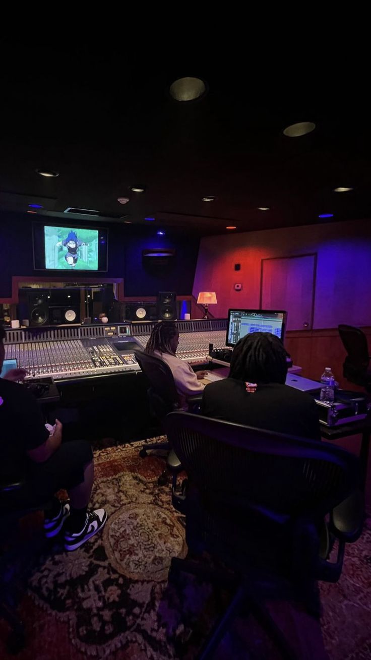 two people sitting in front of a sound board with monitors on the wall behind them