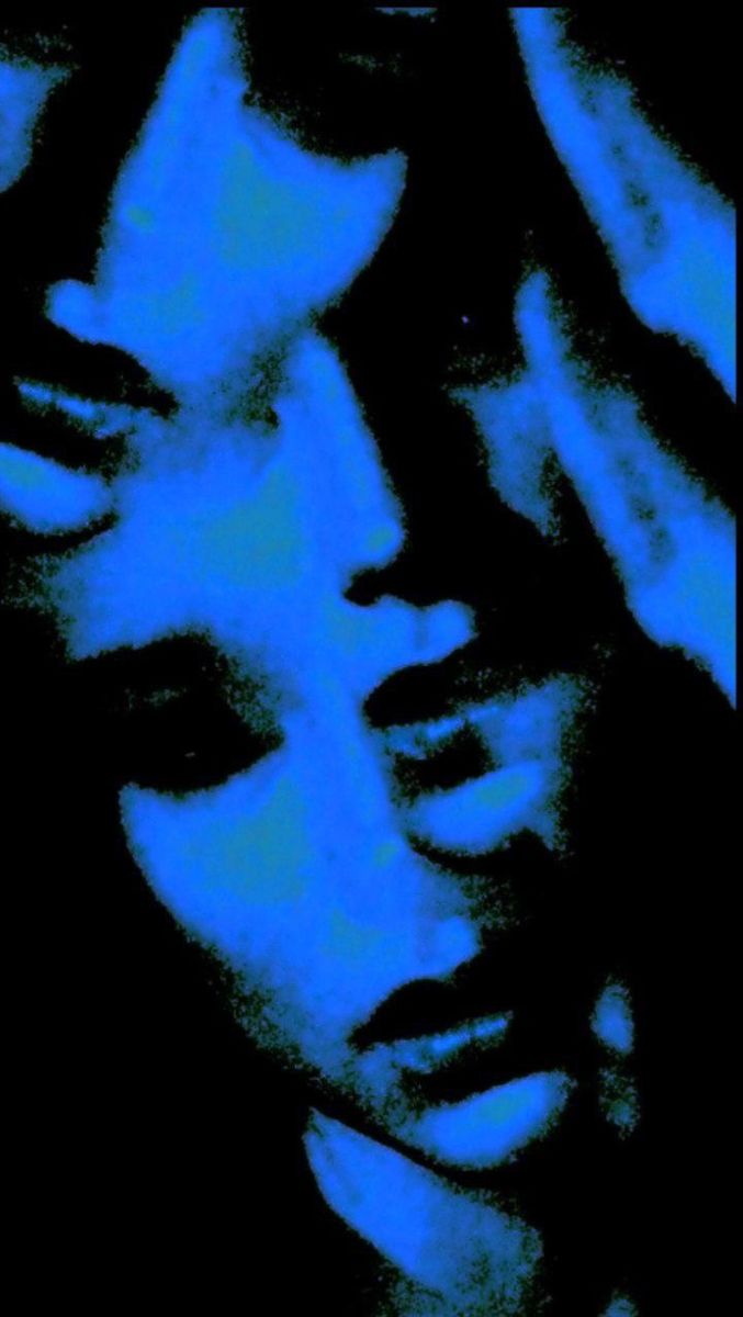 a woman's face is lit up with blue light in the dark, and she has her hands on her head