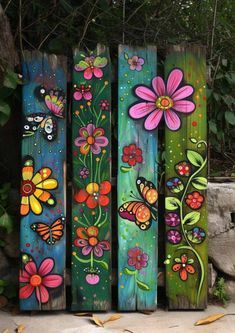 four painted wooden planks with flowers and butterflies on them, sitting in front of a stone wall