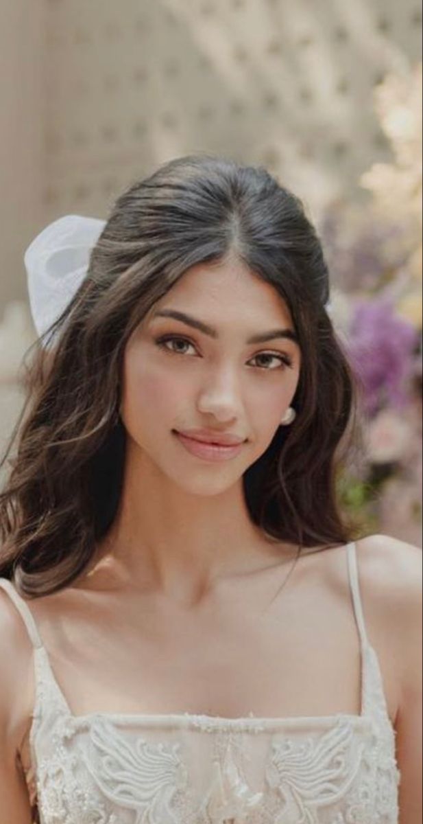 a woman with long hair wearing a white dress and a bow in her hair is smiling at the camera