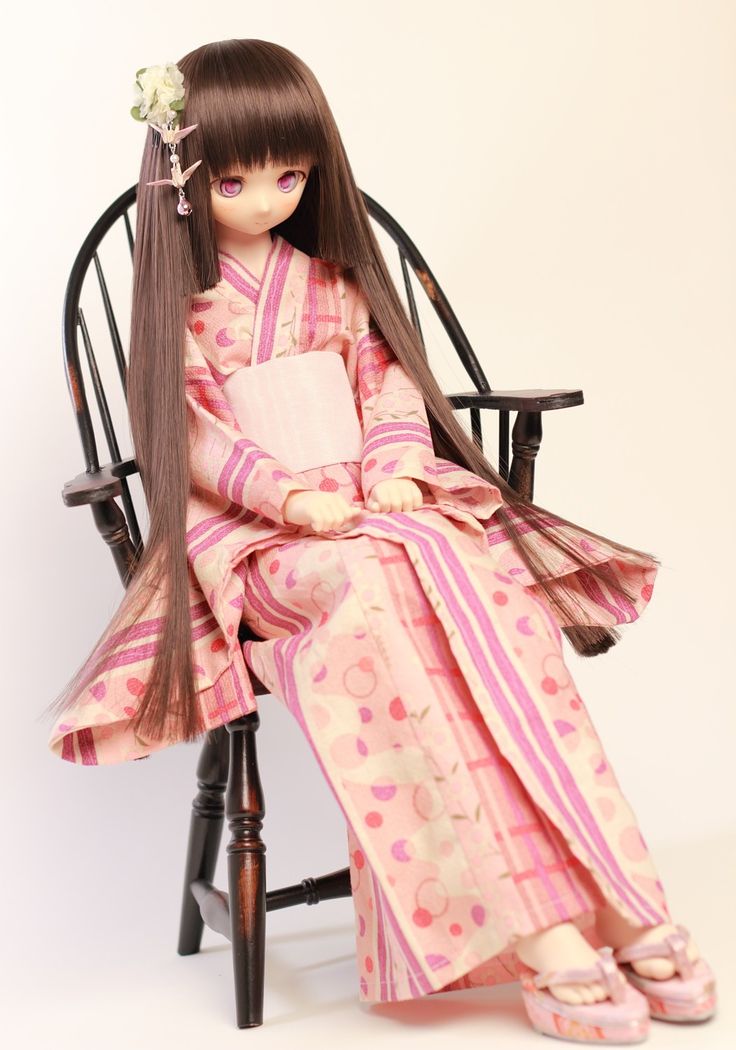 a doll sitting in a chair wearing a pink and white kimono with long hair