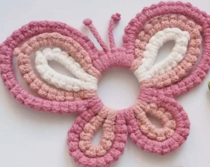 a crocheted pink and white butterfly sitting on top of a table next to flowers