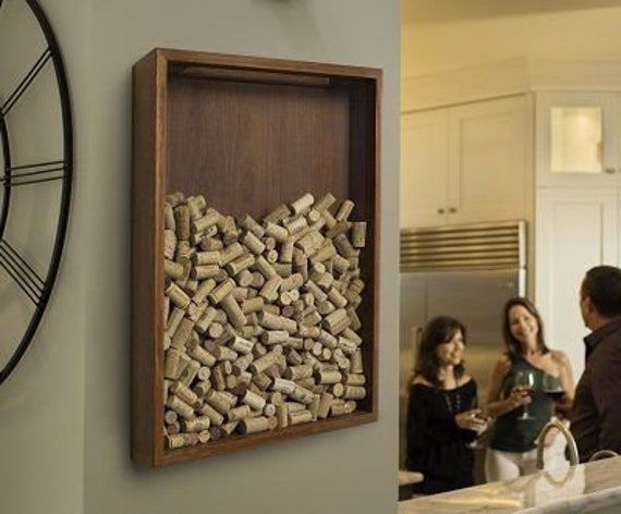 two people standing in a kitchen next to a wall mounted wine bottle corks holder