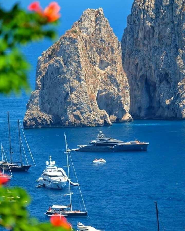 several boats are in the water near some rocks and cliffs, with one boat on the other side