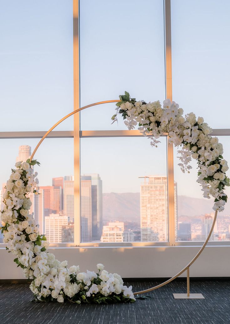 a circular floral arrangement in front of a window with cityscape and skyscrapers behind it