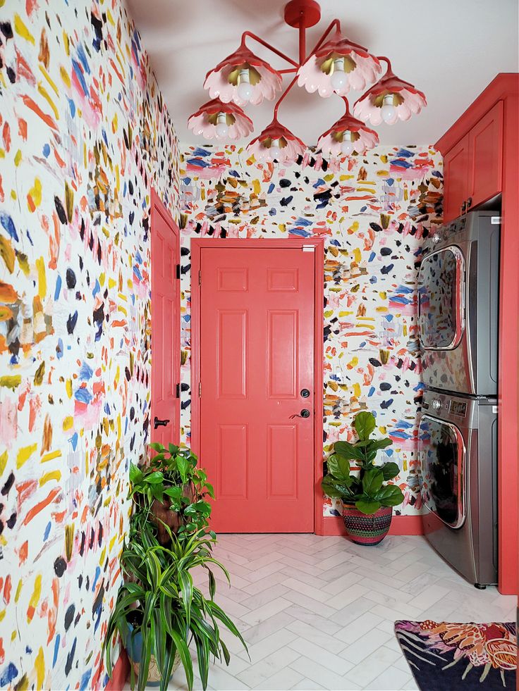 a kitchen with red doors and colorful wallpaper on the walls, potted plants in front of an orange door