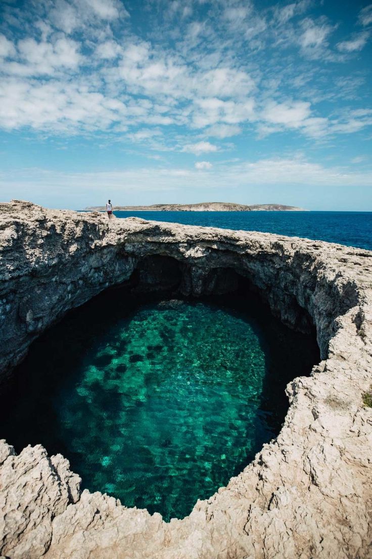 a man standing on top of a rocky cliff next to the ocean with a blue hole in it