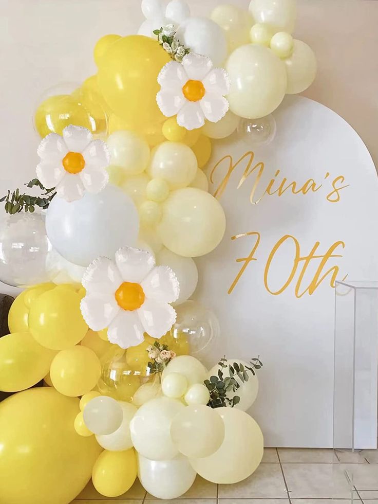 the balloon arch is decorated with white and yellow balloons, daisies and greenery