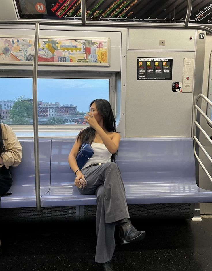 two women are sitting on a subway train and one is talking on her cell phone