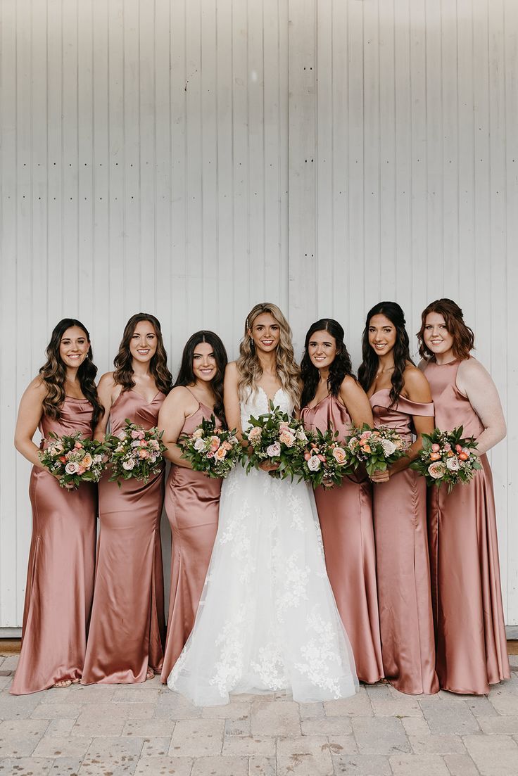 a group of women standing next to each other in front of a white wall holding bouquets