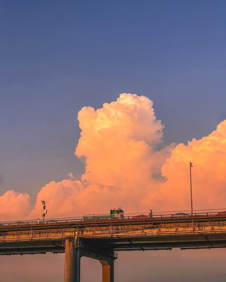 a train traveling over a bridge with clouds in the sky behind it and traffic lights on either side