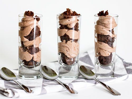 three glasses filled with desserts sitting on top of a table next to spoons