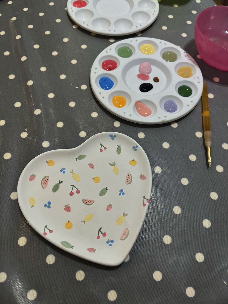 two heart shaped plates with paintbrushes sitting on a polka dot covered tablecloth