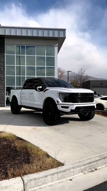 a white truck is parked in front of a building with large windows and black rims