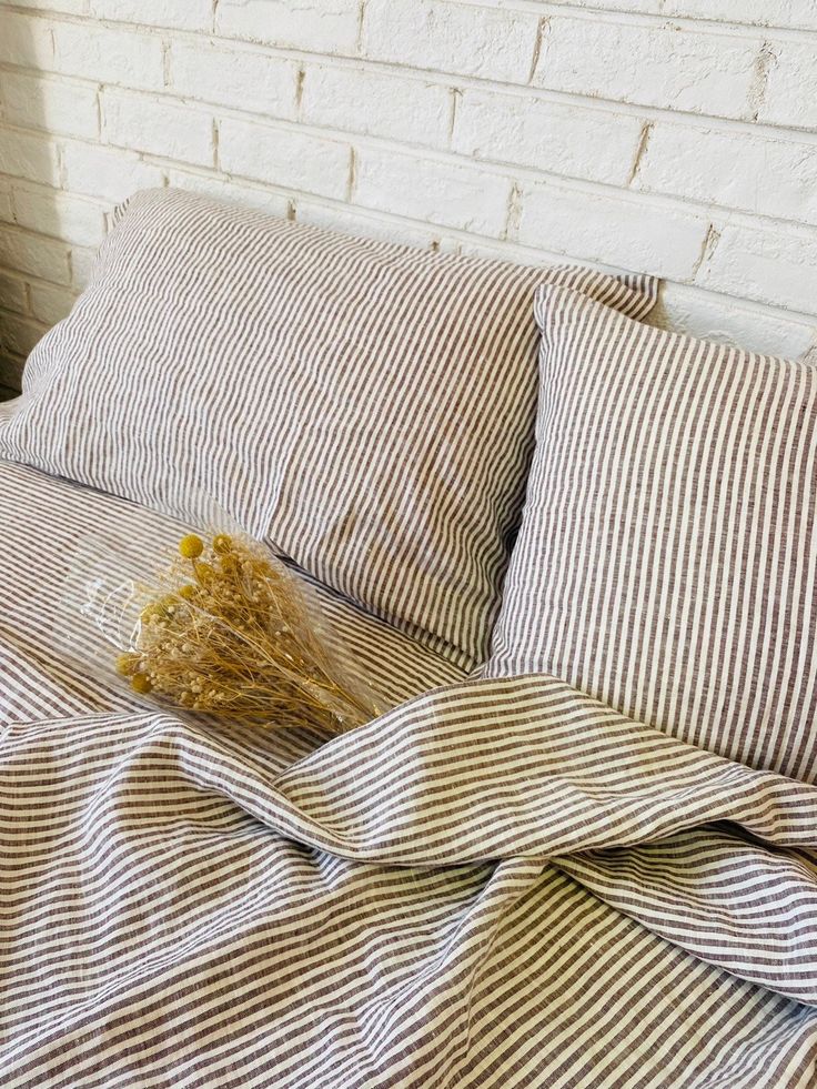 an unmade bed with striped linens and a dried plant on the pillowcase