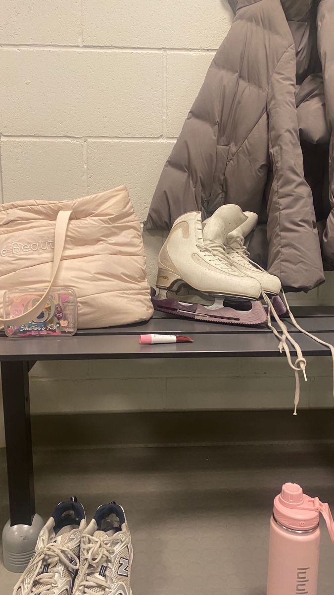 shoes and other items sit on a bench in front of a coat, jacket, and water bottle