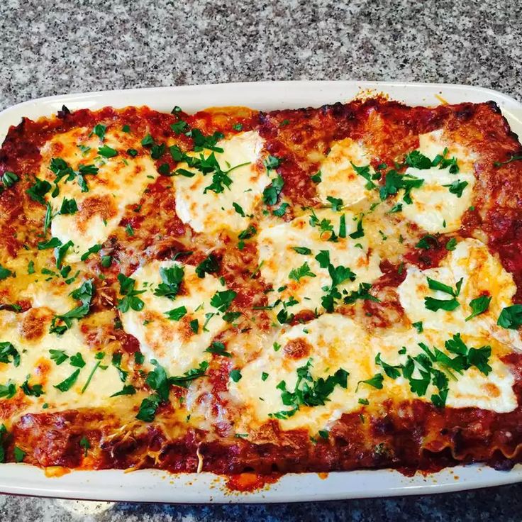 a square casserole dish with cheese and parsley on the top, ready to be eaten