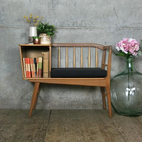 a wooden bench sitting next to a glass vase filled with flowers and books on top of a hard wood floor