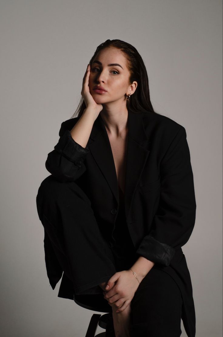 a woman sitting on top of a chair wearing a black suit