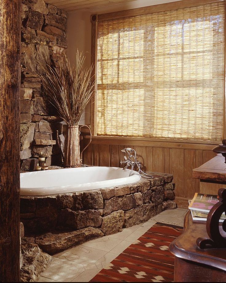 a bathroom with stone walls and a large bathtub next to a window covered in bamboo blinds