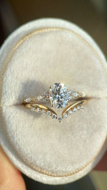 a person holding a ring with two diamonds on it in a velvet display case that is white and gold