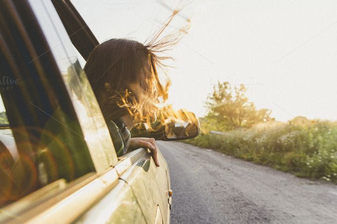 a woman leaning out the window of a car on a country road with her hair blowing in the wind