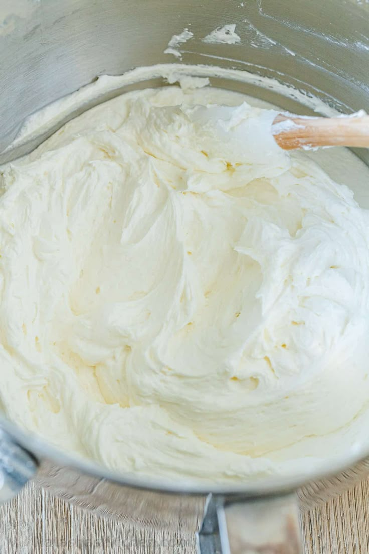 a metal bowl filled with white frosting on top of a wooden table