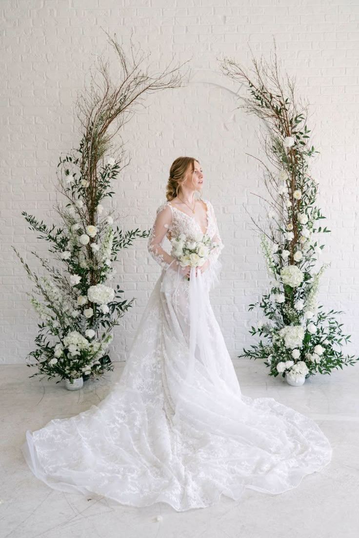 a bride standing in front of an arch with flowers and greenery