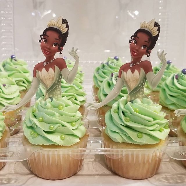 cupcakes decorated with green frosting and princess silhouettes on top are displayed in plastic trays