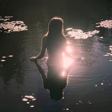 a woman is sitting in the water with her back turned to the camera and sun shining behind her