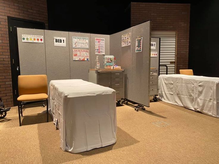 an empty room with chairs and tables covered in white cloths next to a brick wall