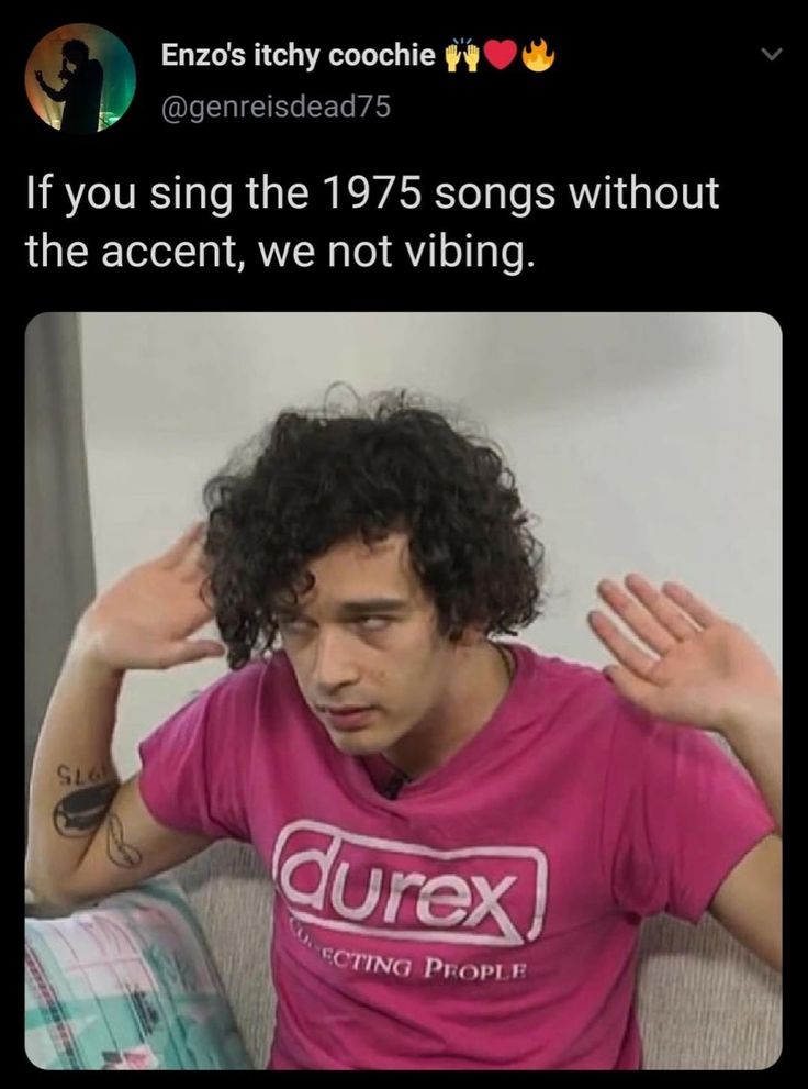 a man with curly hair wearing a pink shirt and holding his hands up to his head