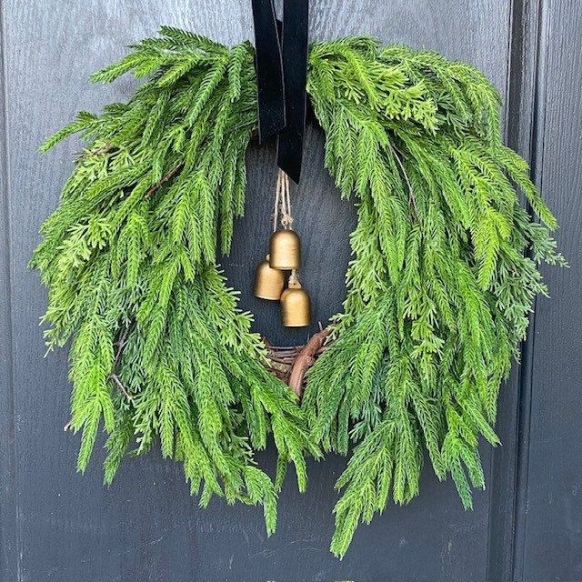 a wreath with two bells hanging from it's side on the front door,