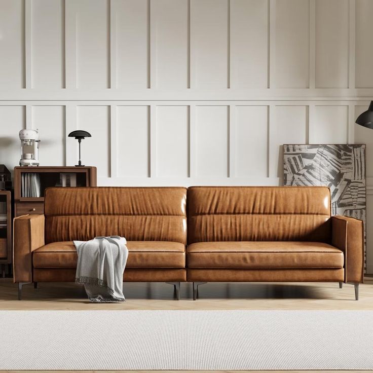 a brown leather couch sitting on top of a wooden floor next to a book shelf