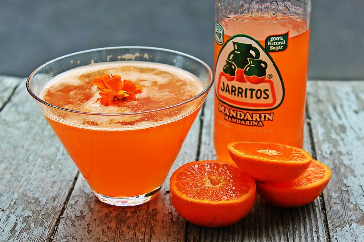 an orange drink next to sliced oranges on a wooden table