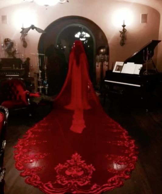 a red wedding dress is on display in a room with piano and chairs, along with other furniture