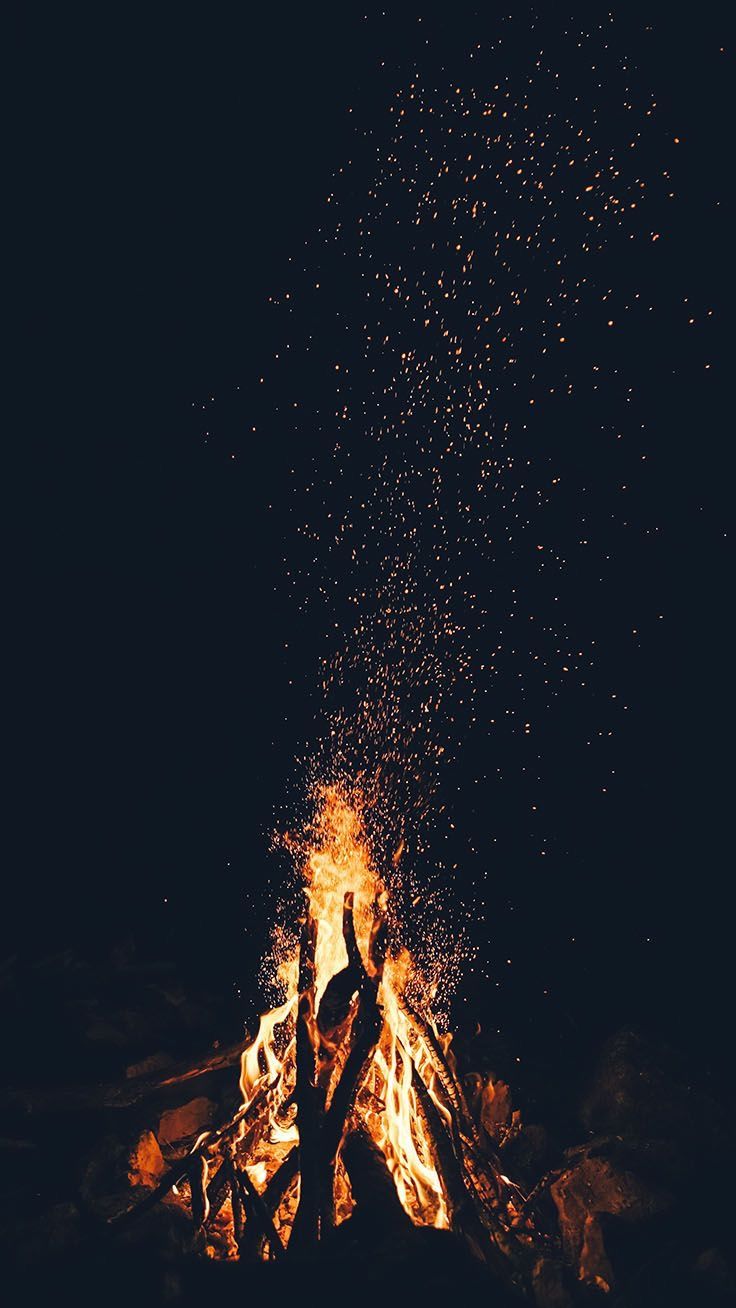 two people standing in front of a campfire with lots of fire and sparks coming out of it