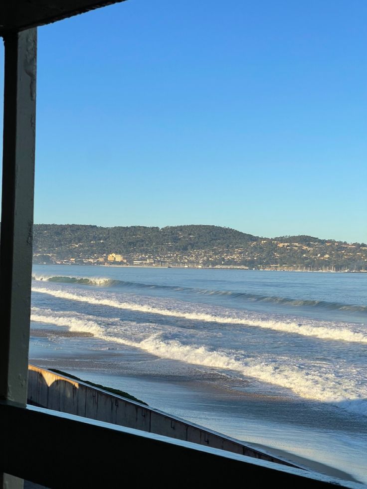 the view from inside a house looking out at the ocean and hills in the distance