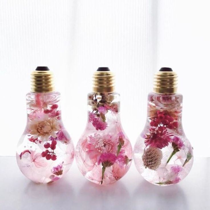 three glass vases with flowers in them on a white surface, one is gold and the other is pink