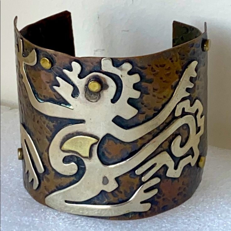 a close up of a metal bracelet on a white surface with an ornate design in the middle