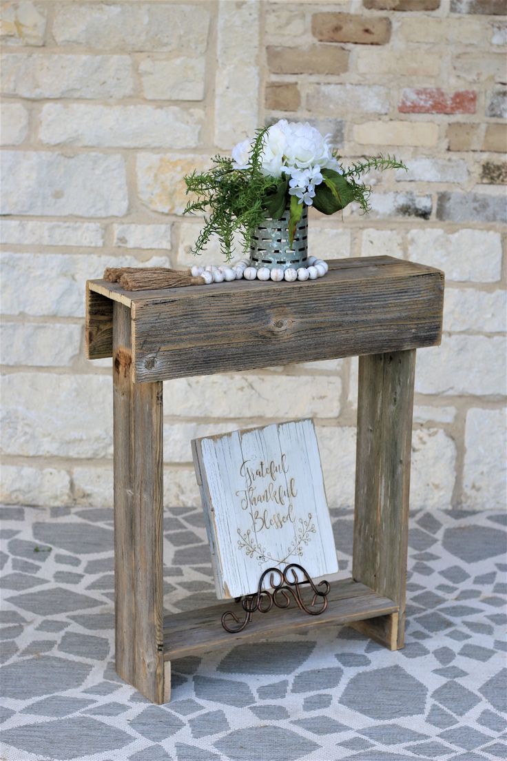 a small wooden table with a sign and flowers on top, sitting in front of a brick wall