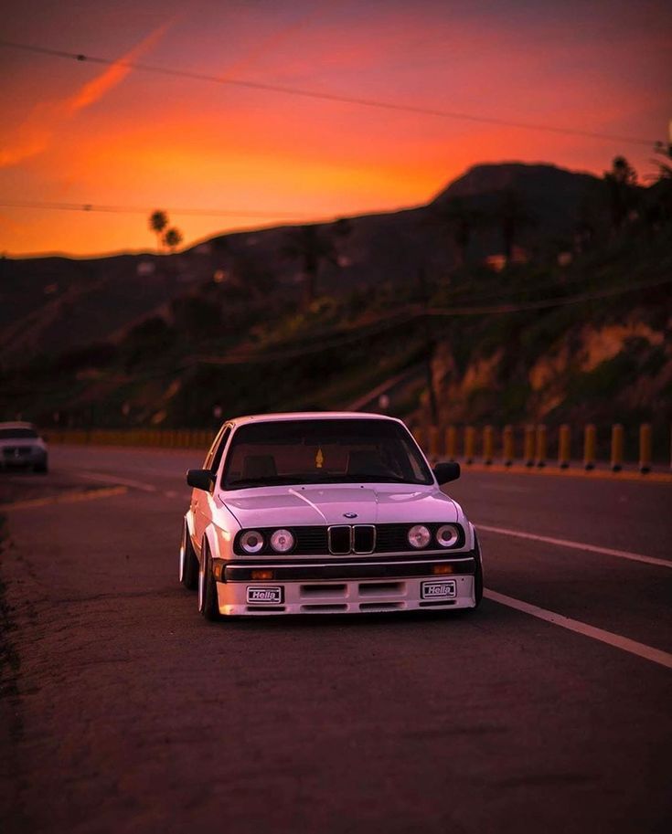 a white car is parked on the side of the road in front of an orange sunset