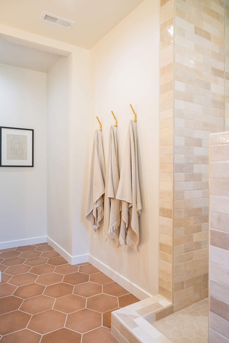 three beige towels hanging on the wall in a bathroom with tiled flooring and white walls