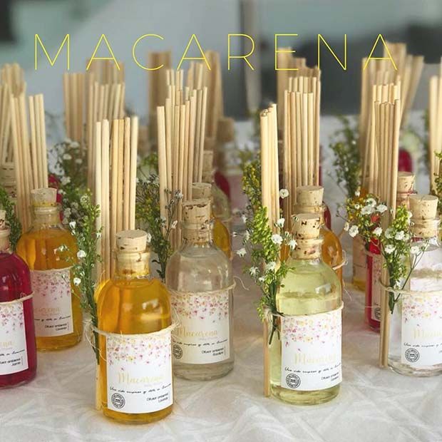 many different types of candles and bottles on a white table cloth with flowers in them