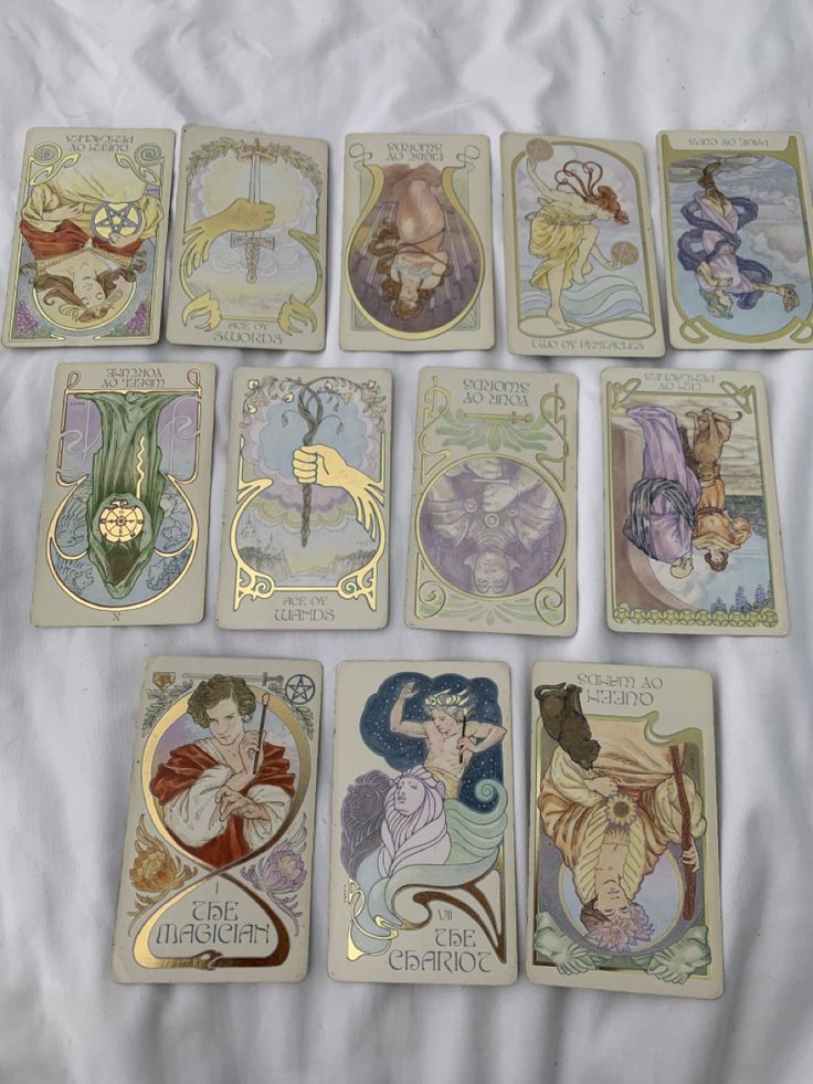 seven different tarot cards are arranged on a white sheet with gold trimmings