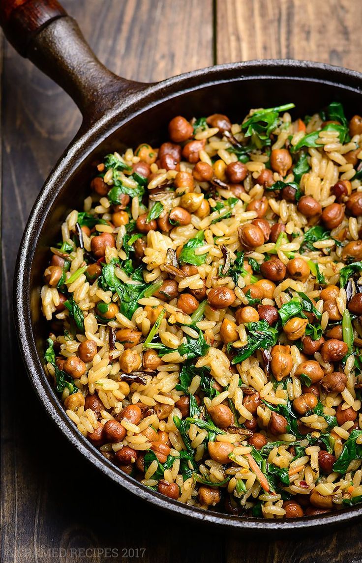 a skillet filled with rice, beans and spinach on top of a wooden table