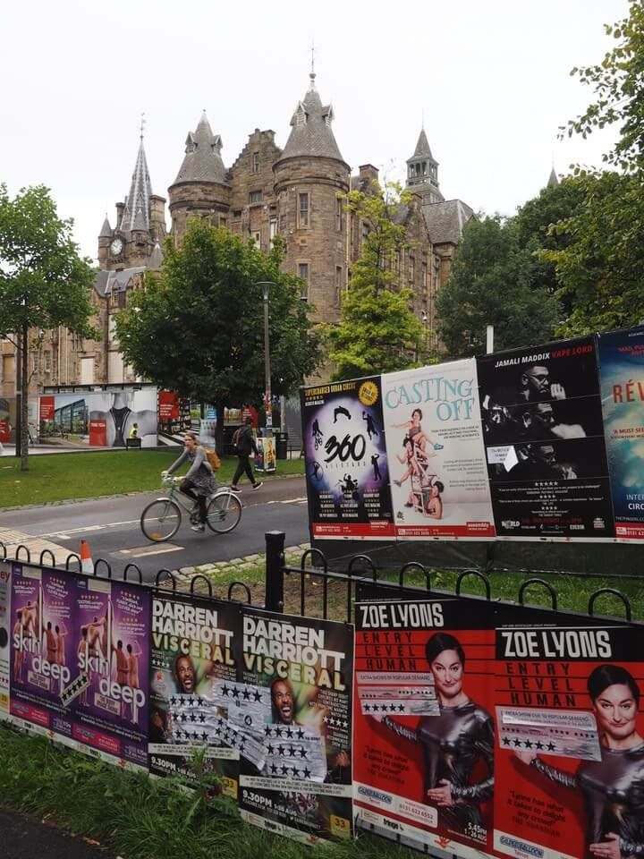 a fence with posters on it and people riding bikes in the distance near some buildings