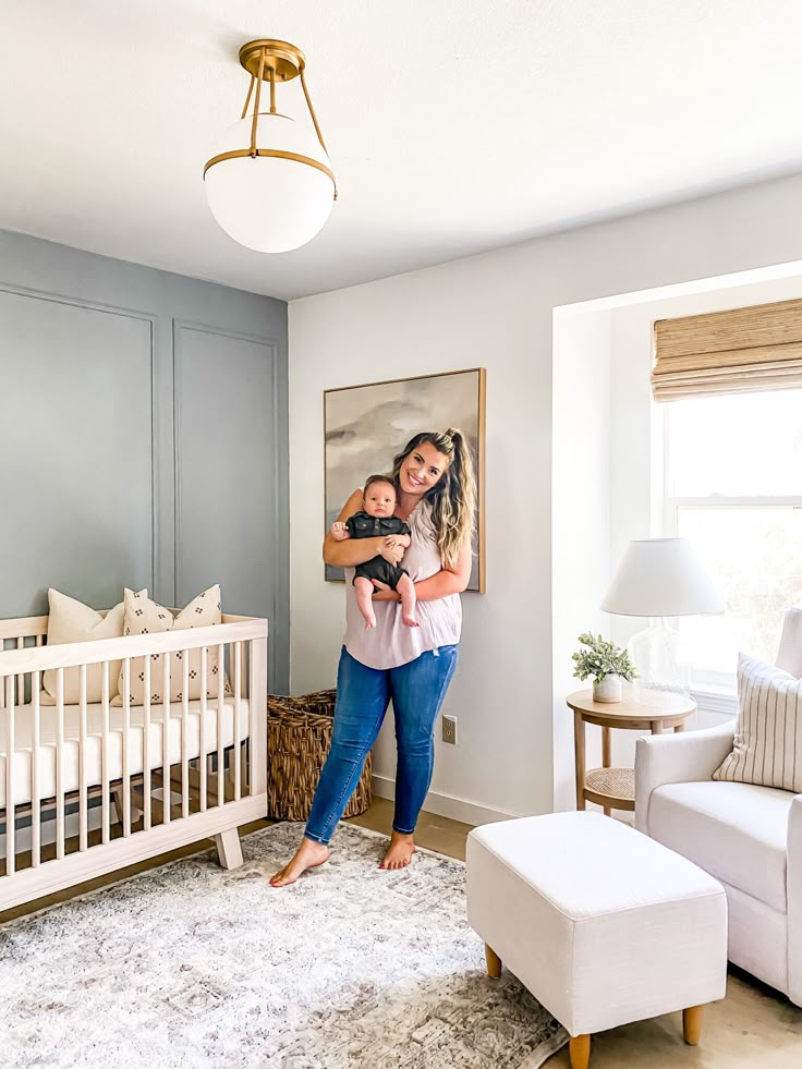 a woman holding a baby in her arms while standing next to a white crib