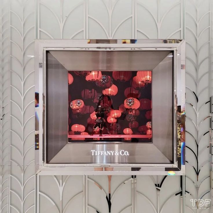 a display case with red lanterns in the middle and white wall paper behind it that says tiffany co